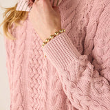 Close-up of a person wearing a pink cable knit sweater with a gold bracelet.