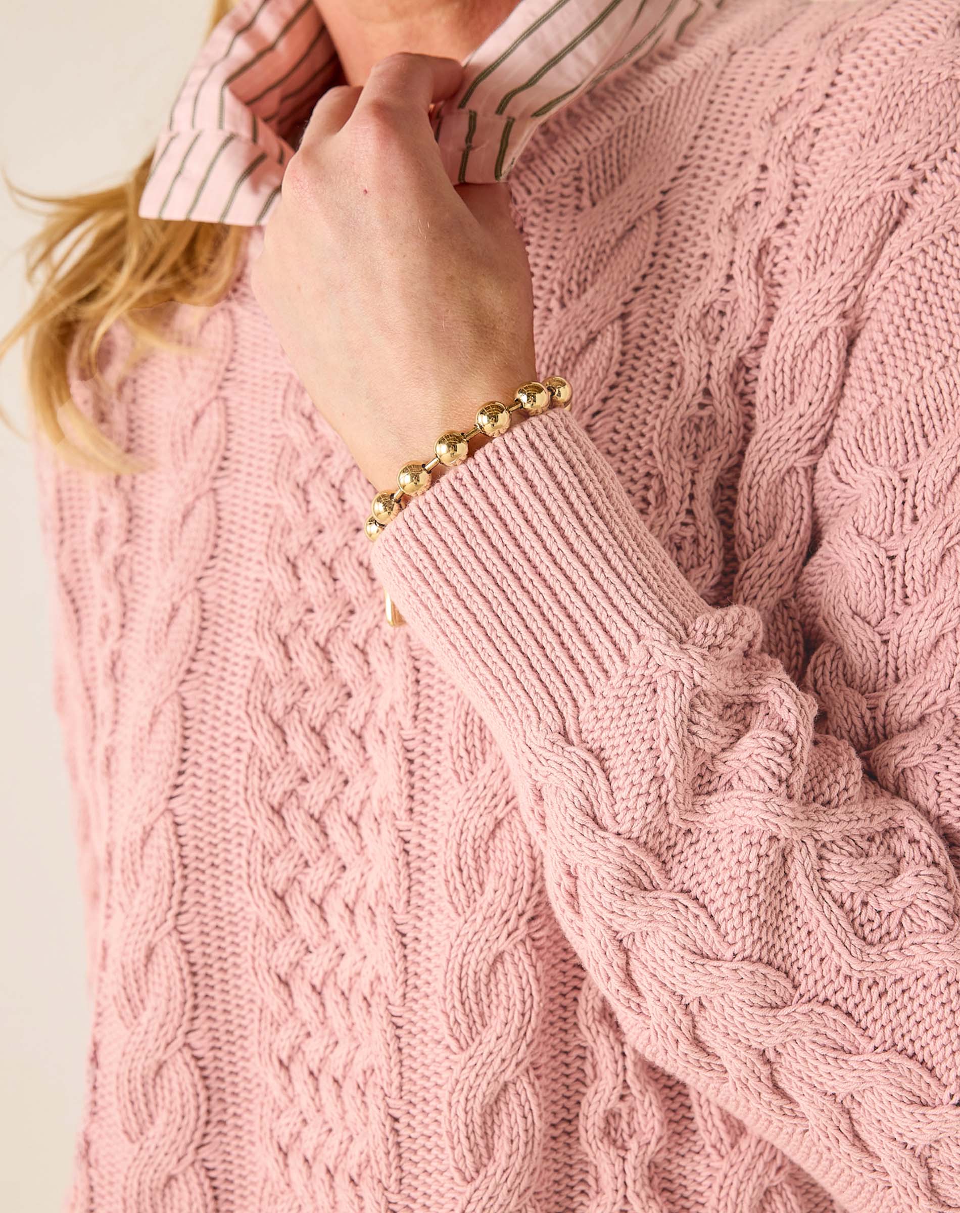 Close-up of a person wearing a pink cable knit sweater with a gold bracelet.