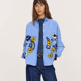 Women's travel-friendly light blue and white striped button-down shirt featuring large embroidered yellow and white floral details.