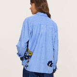 Side view of women's travel-friendly blue and white striped button-down shirt with floral embroidery details.