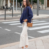 Woman crossing a street wearing a navy sweater, white pants, and white sneakers.