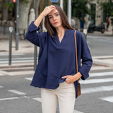 Woman in a blue top and white pants standing on a city street.