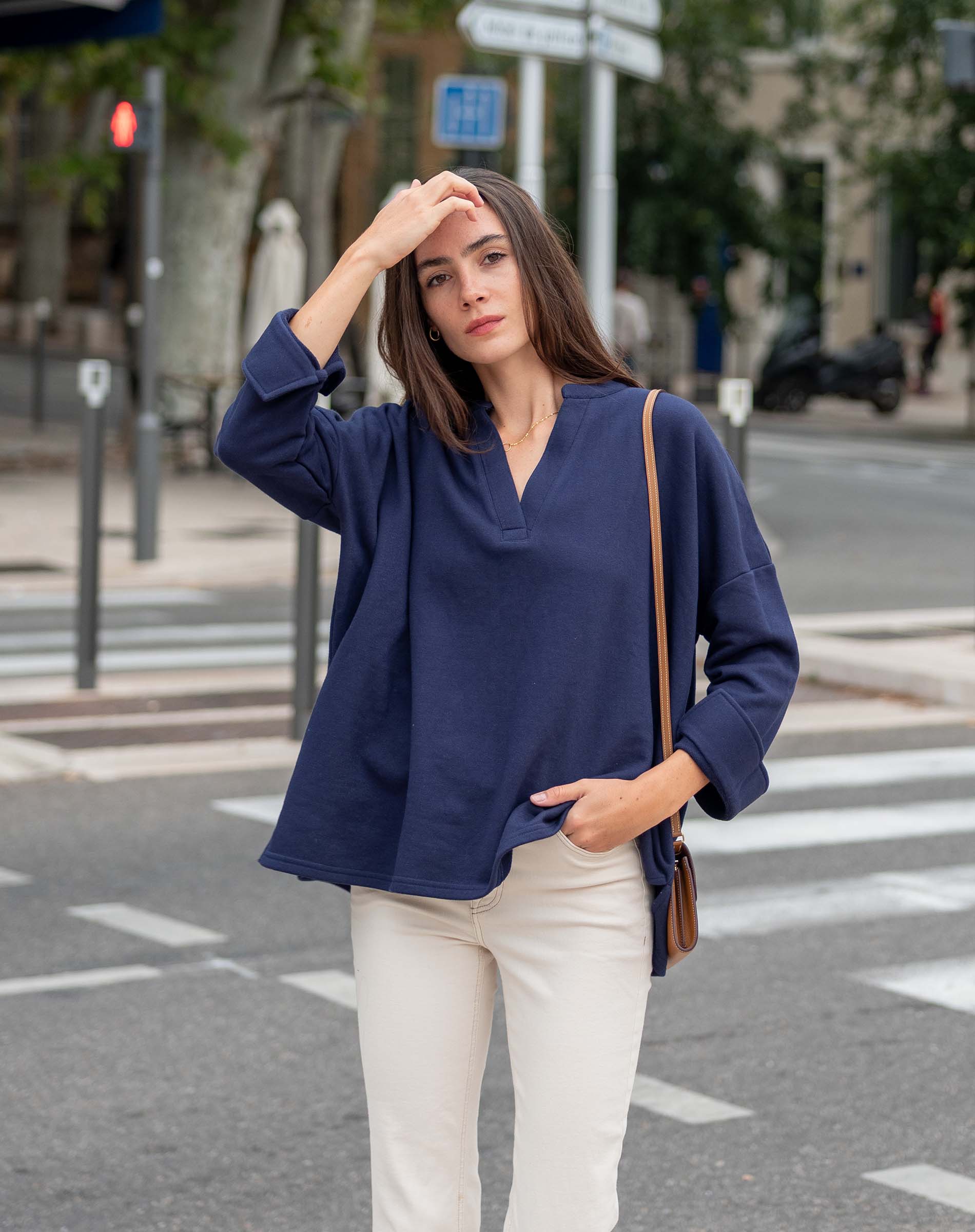 Woman in a blue top and white pants standing on a city street.
