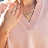 Person wearing a gold necklace with three beads on a light pink top.