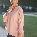 Woman wearing a light pink hoodie outdoors on a sunny day