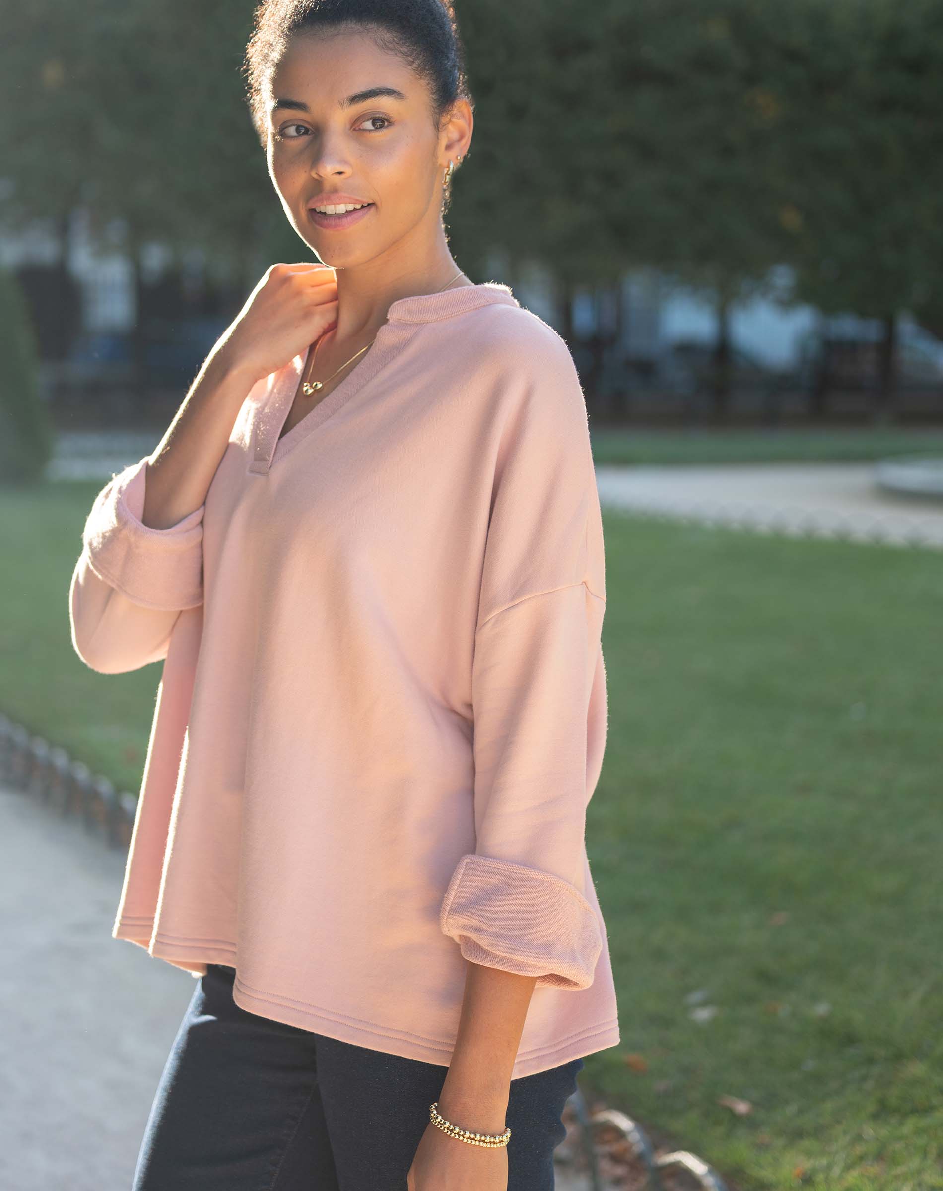 Woman wearing a light pink hoodie outdoors on a sunny day