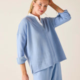 Woman wearing a light blue outfit with a white shirt underneath on a plain background