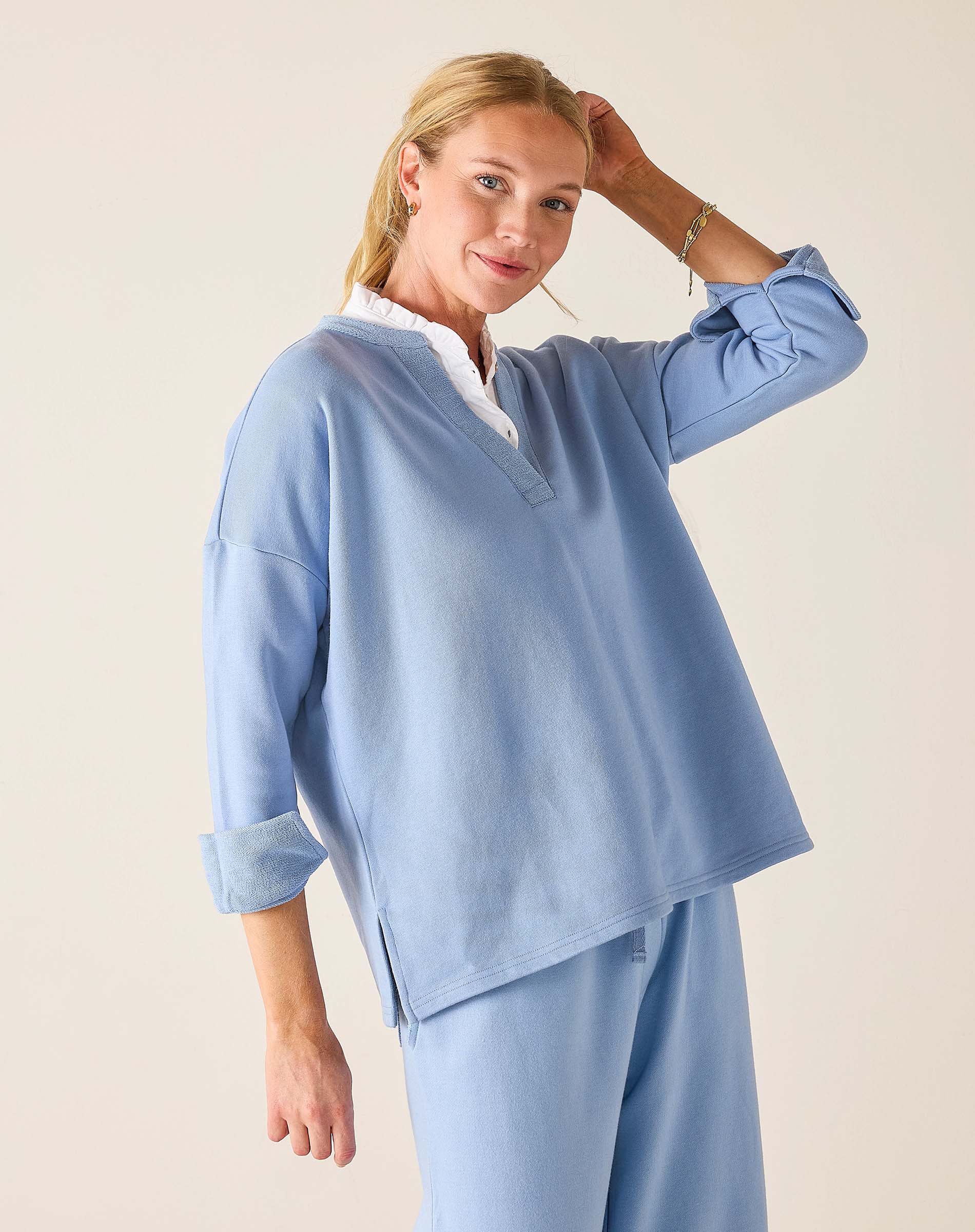 Woman wearing a light blue outfit with a white shirt underneath on a plain background