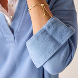 Close-up of a person wearing a blue sweater with rolled-up sleeves and a gold bracelet.