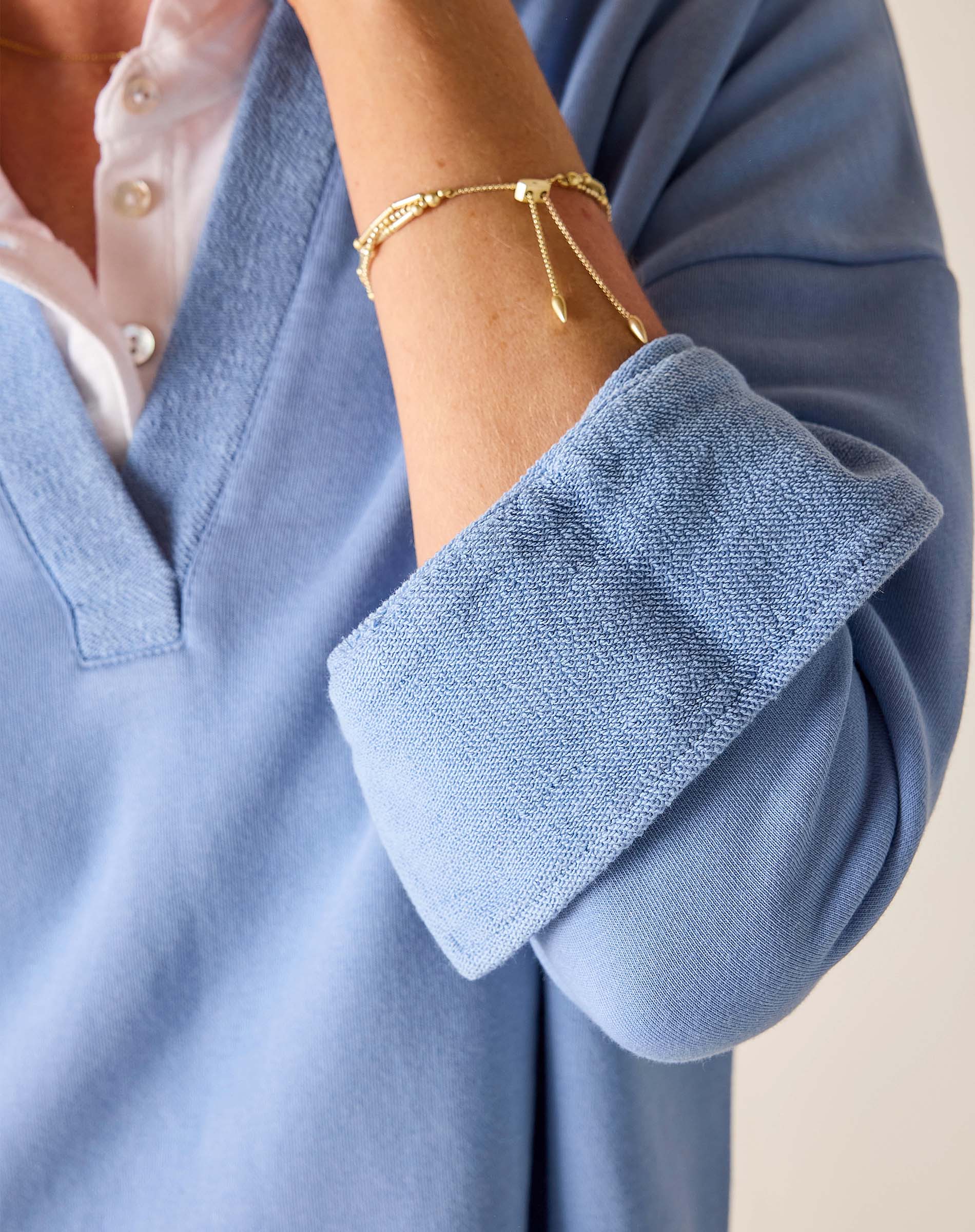 Close-up of a person wearing a blue sweater with rolled-up sleeves and a gold bracelet.
