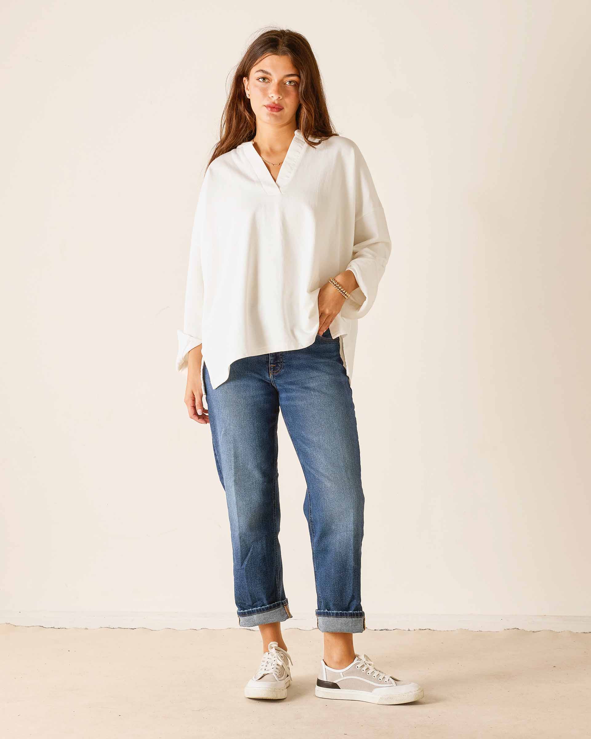 Woman wearing a white blouse and blue jeans against a plain background