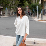 Woman in a white shirt and light blue jeans standing on a street with a brown bag.