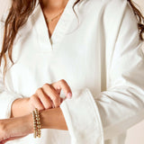Person wearing a white outfit with gold jewelry on a neutral background