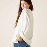 Woman wearing a white blouse and blue jeans against a plain background