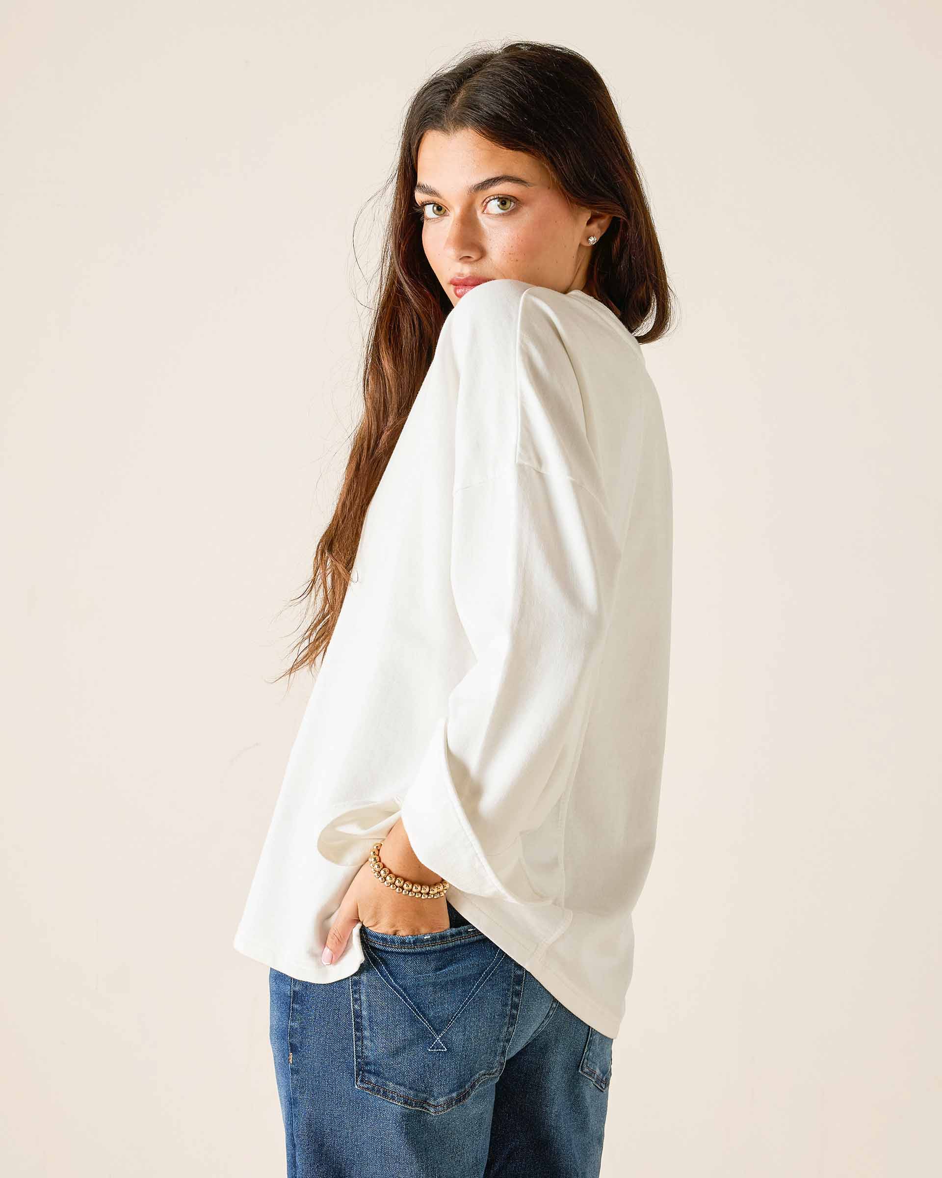 Woman wearing a white blouse and blue jeans against a plain background