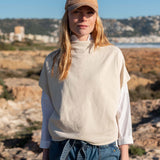 Bone dolman top over a white long-sleeved shirt and blue denim jeans.