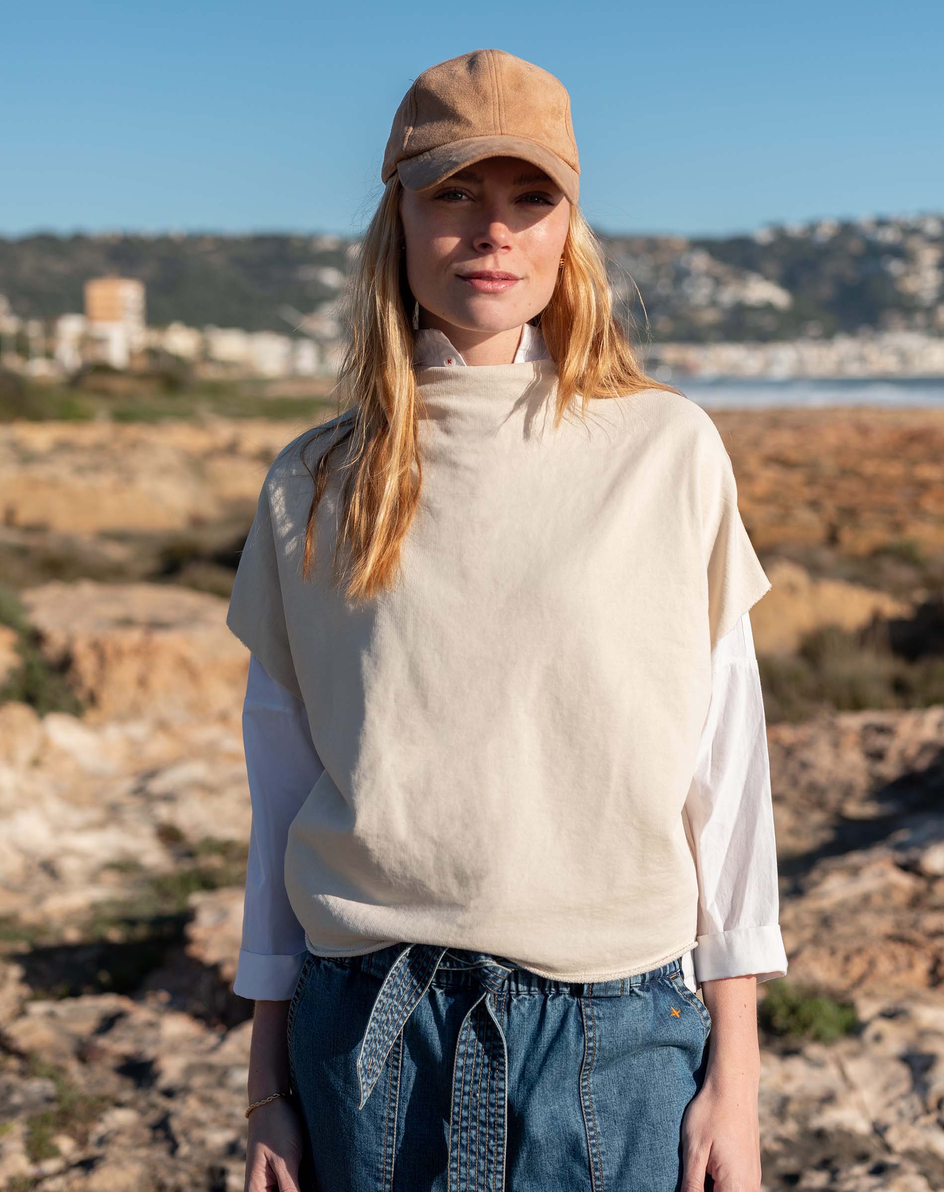 Bone dolman top over a white long-sleeved shirt and blue denim jeans.