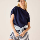 Woman wearing a navy top, striped shorts, and a light blue cap on a beige background