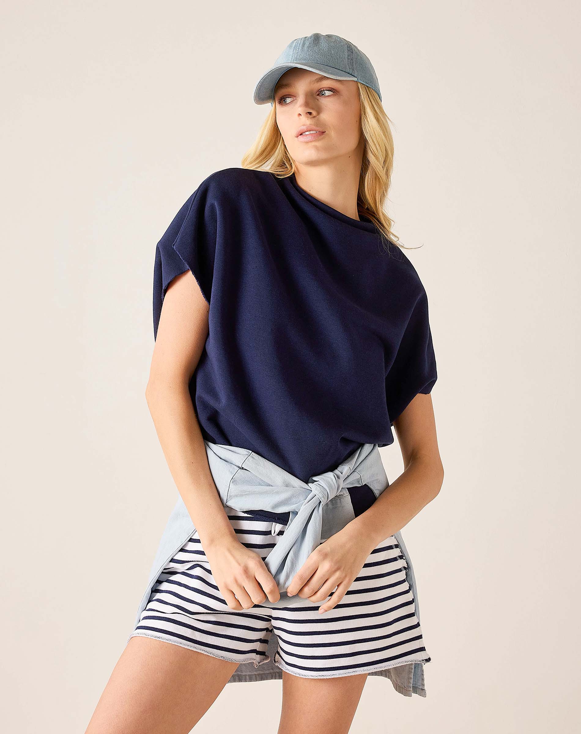 Woman wearing a navy top, striped shorts, and a light blue cap on a beige background