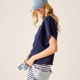 Woman wearing a navy blue top, striped shorts, and a denim cap on a beige background