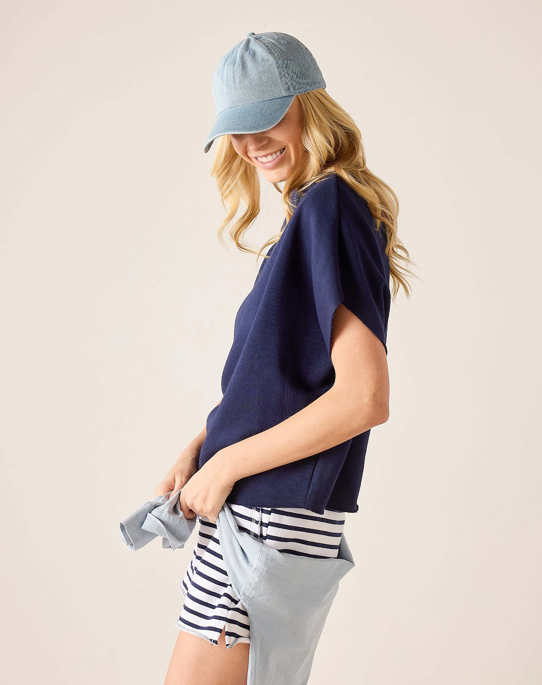 Woman wearing a navy blue top, striped shorts, and a denim cap on a beige background