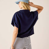 Person wearing a navy blue top and striped shorts with a light blue cap on a beige background