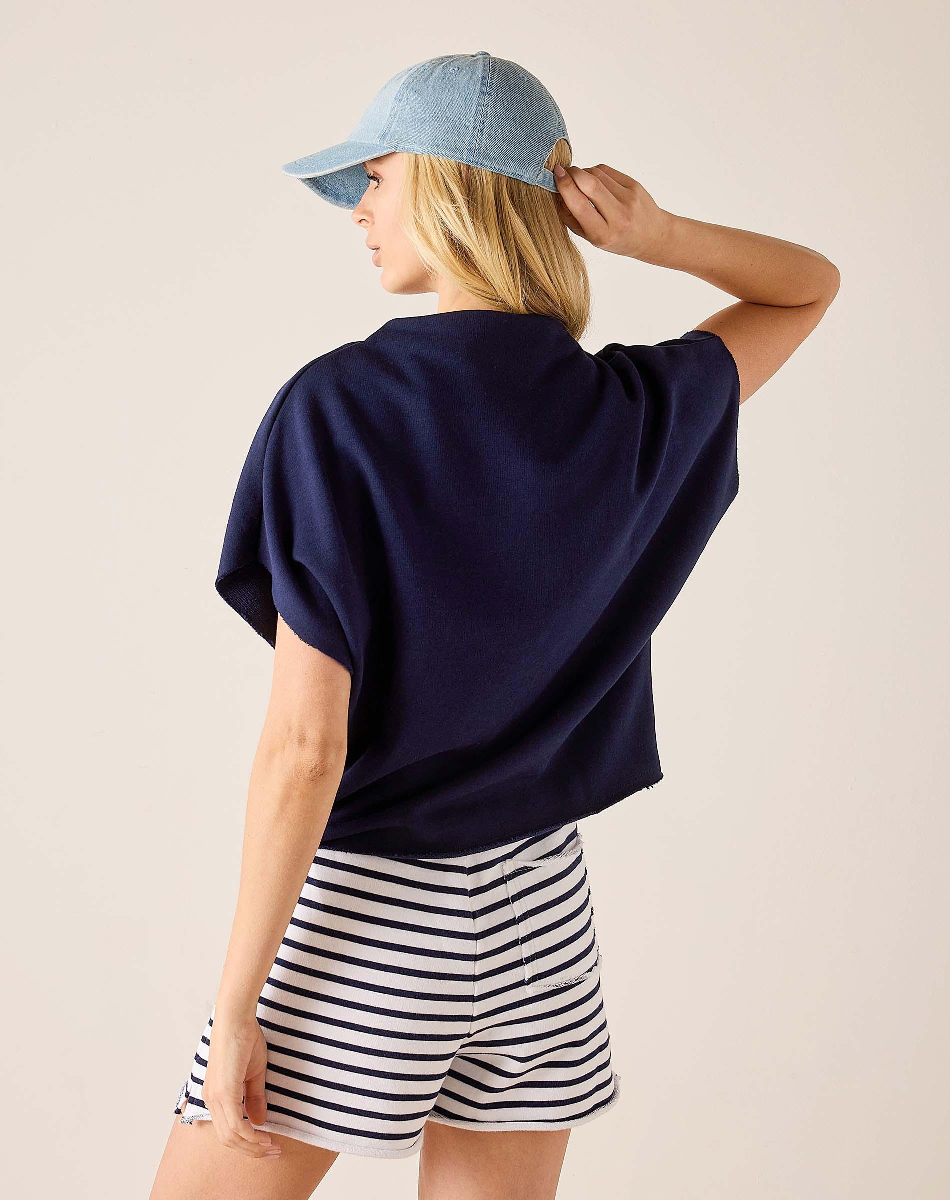 Person wearing a navy blue top and striped shorts with a light blue cap on a beige background