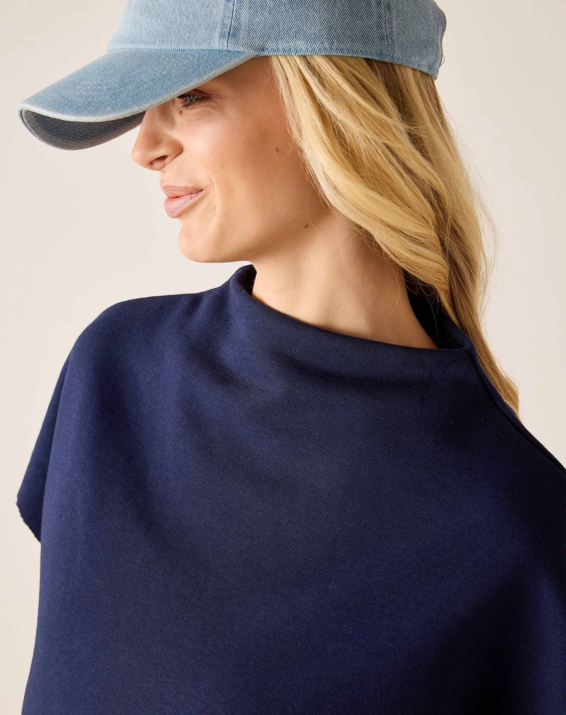 Woman wearing a navy blue top and denim cap on a plain background