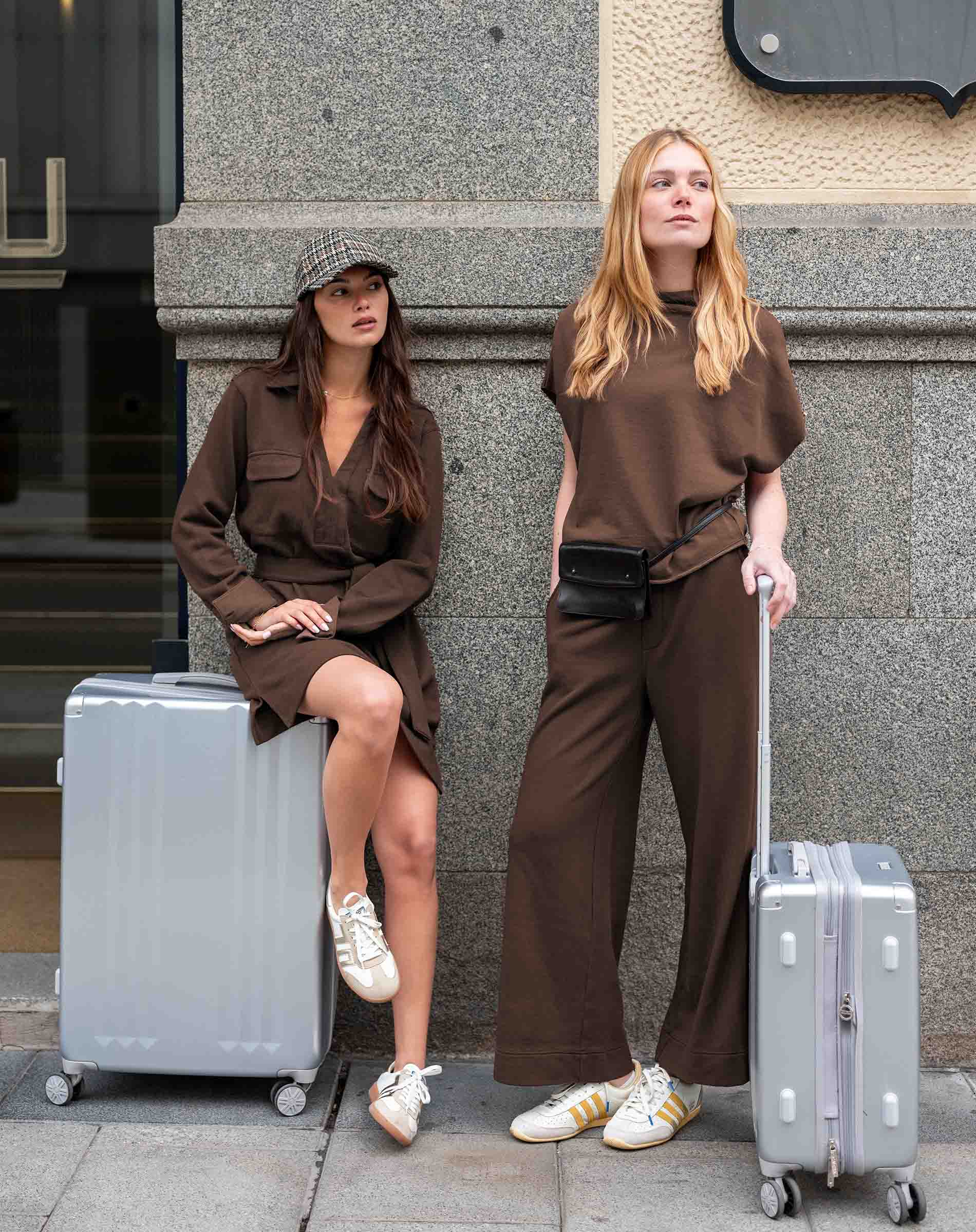MERSEA women's travel-friendly espresso dolman top and wide-leg trousers worn by two women with suitcases.