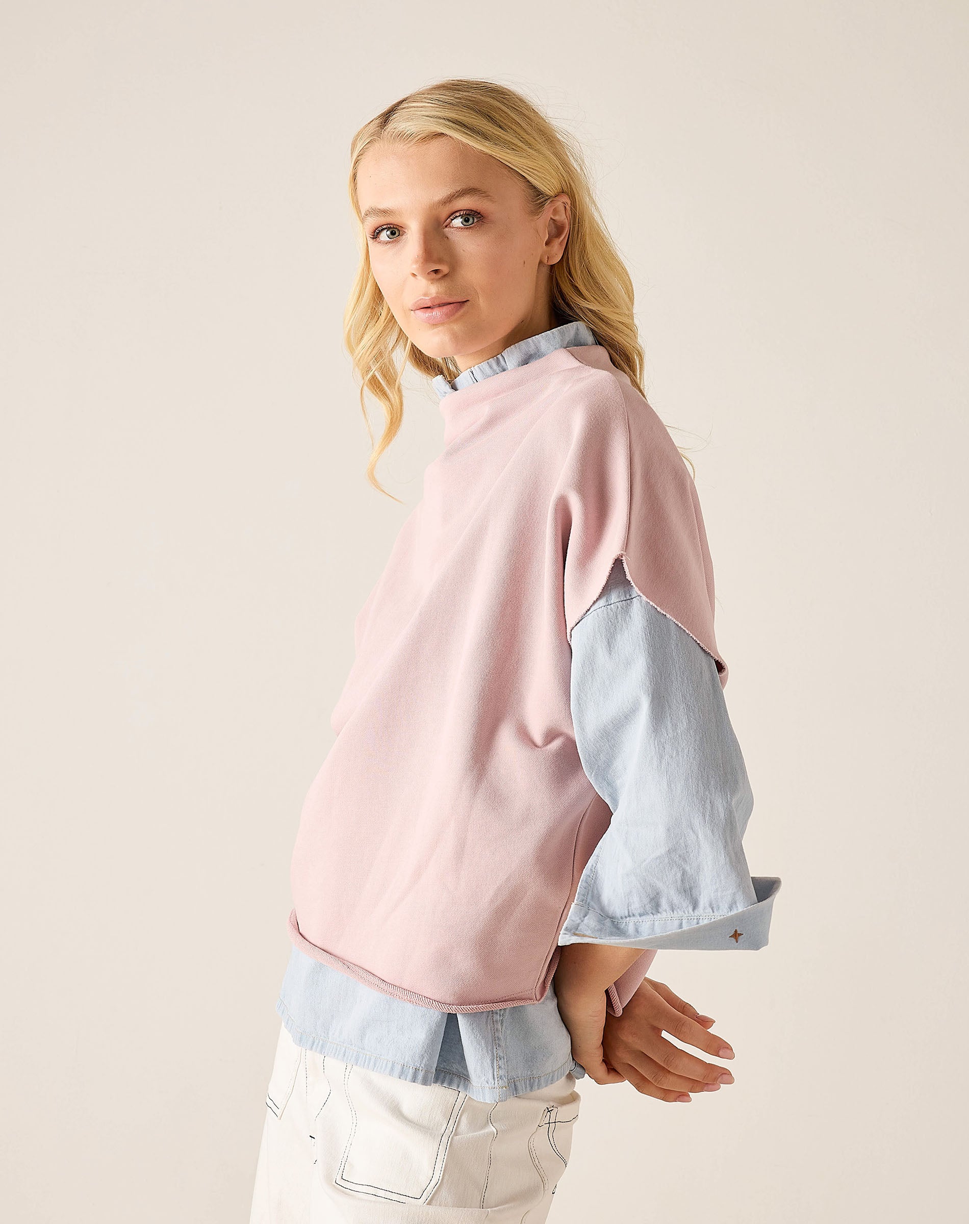 Woman wearing a pink and denim color-blocked sweater on a beige background