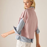 Woman wearing a pink sweater over a blue shirt with beige pants on a plain background