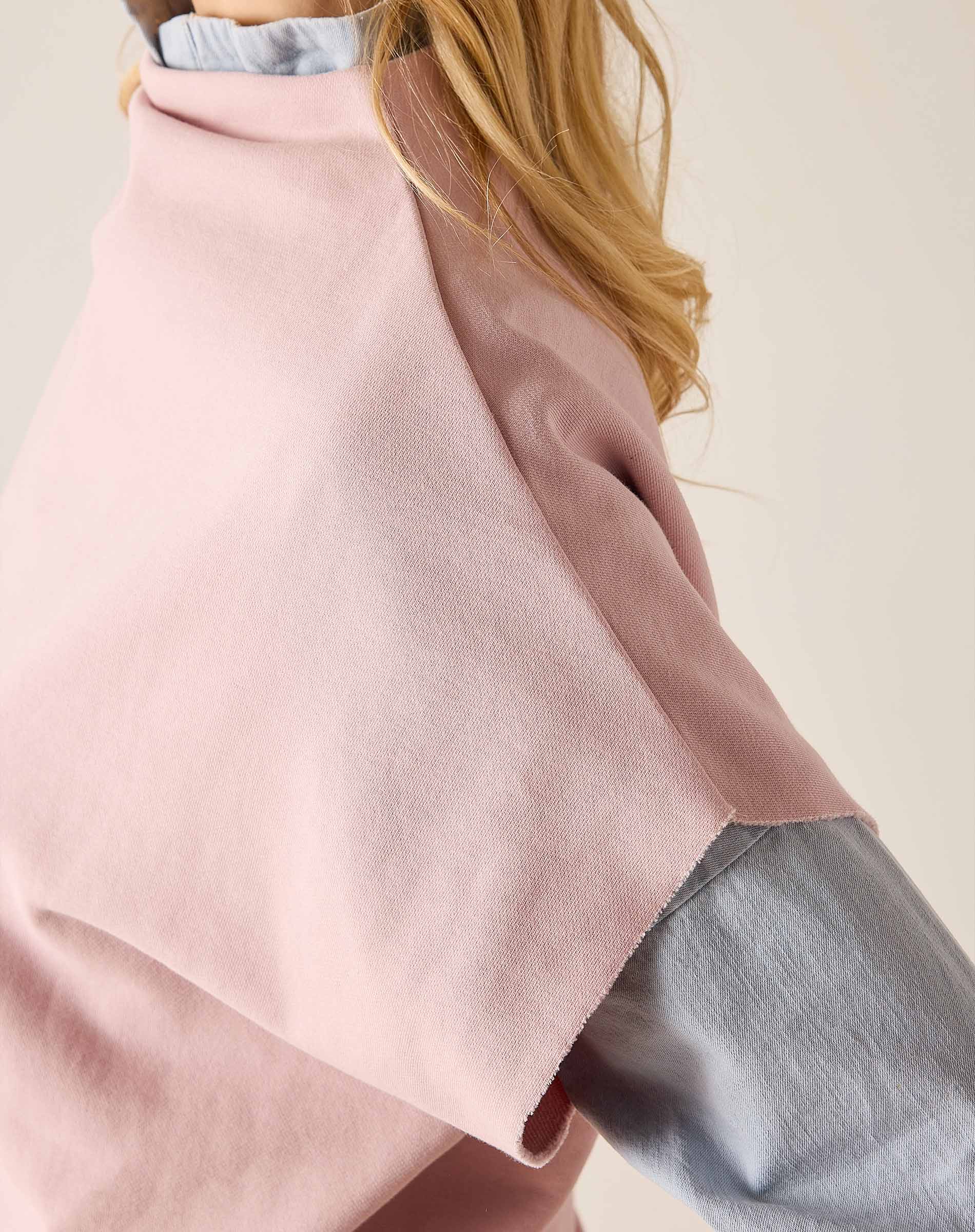 Person wearing a pink poncho over a gray outfit on a plain background