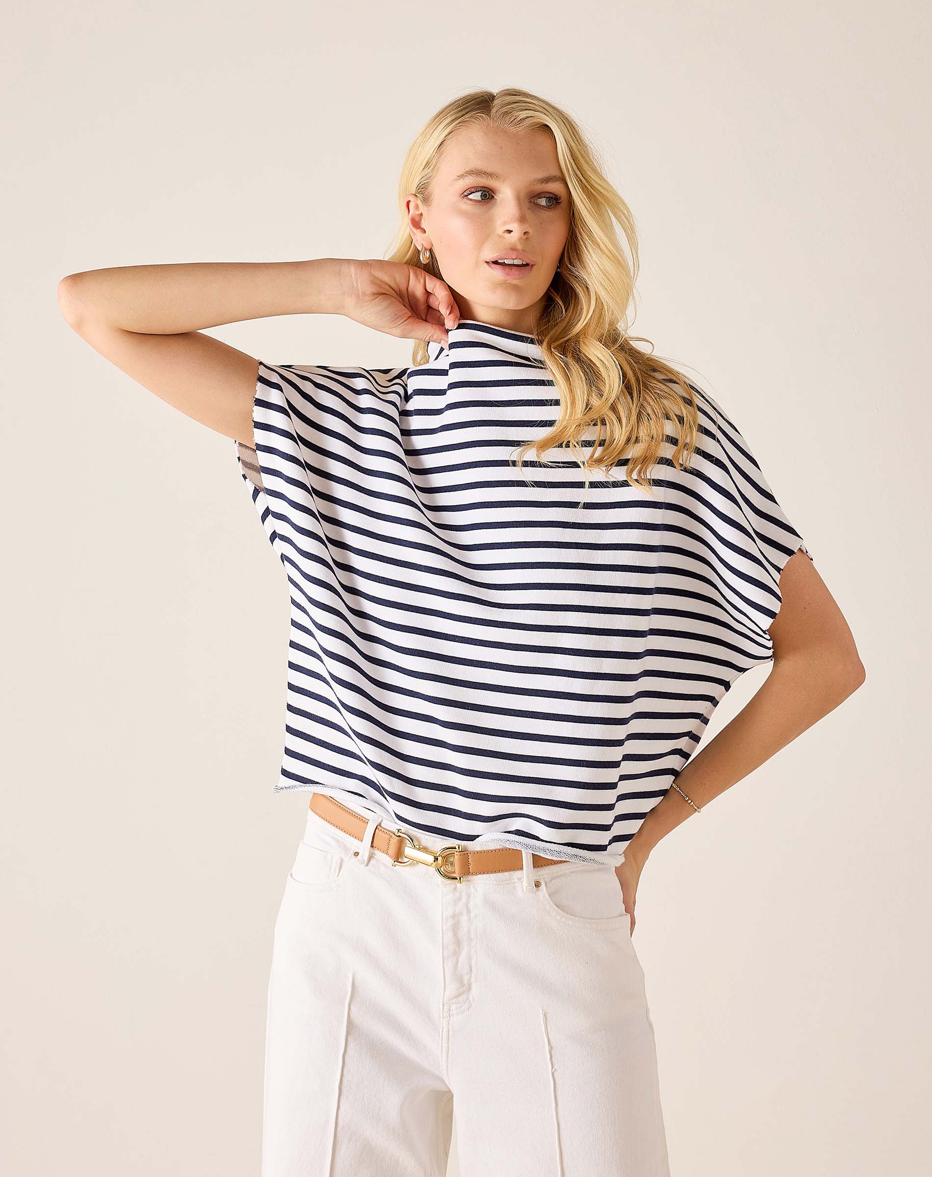 Woman wearing a black and white striped shirt with white pants on a beige background