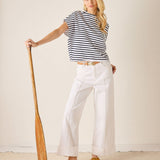 Woman in a striped shirt and white pants holding a paddle against a plain background