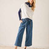 Woman wearing a white sweater with blue sleeves and blue jeans on a plain background