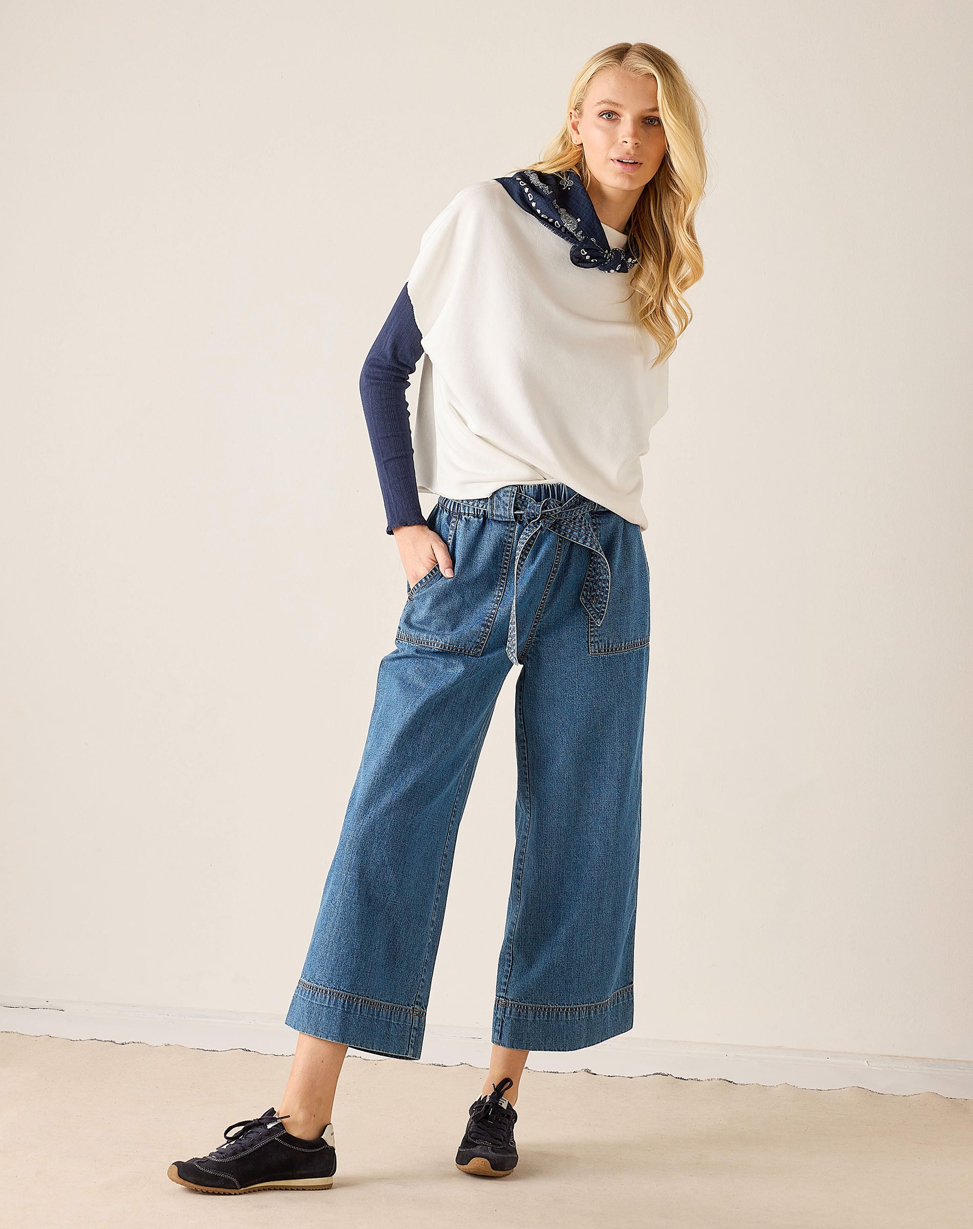Woman wearing a white sweater with blue sleeves and blue jeans on a plain background