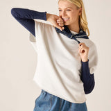 Woman wearing a white and navy long-sleeve shirt with denim pants on a beige background