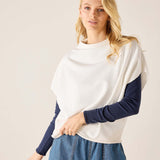 Woman wearing a white and navy long-sleeve top with blue jeans on a plain background