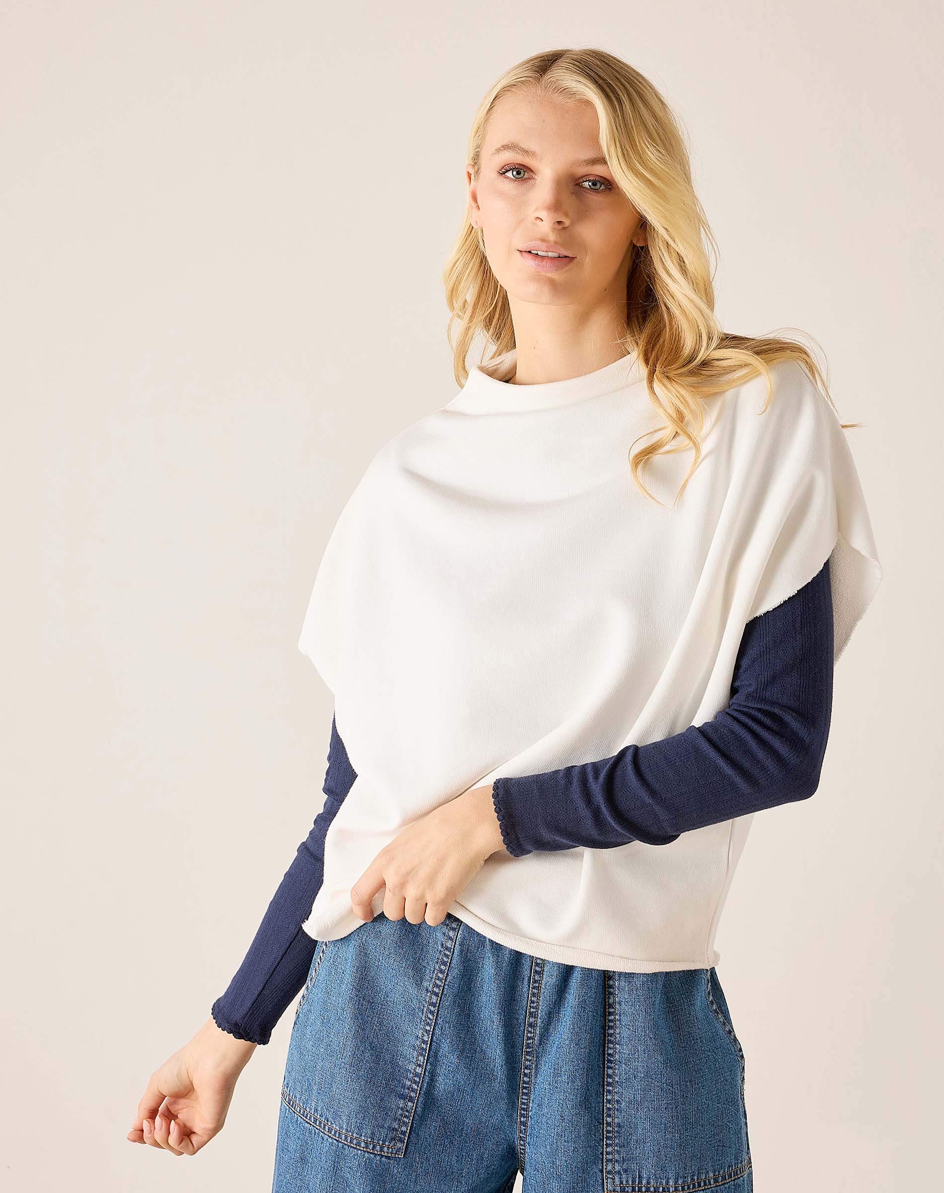 Woman wearing a white and navy long-sleeve top with blue jeans on a plain background
