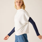 Woman wearing a white top with navy sleeves and blue jeans on a plain background