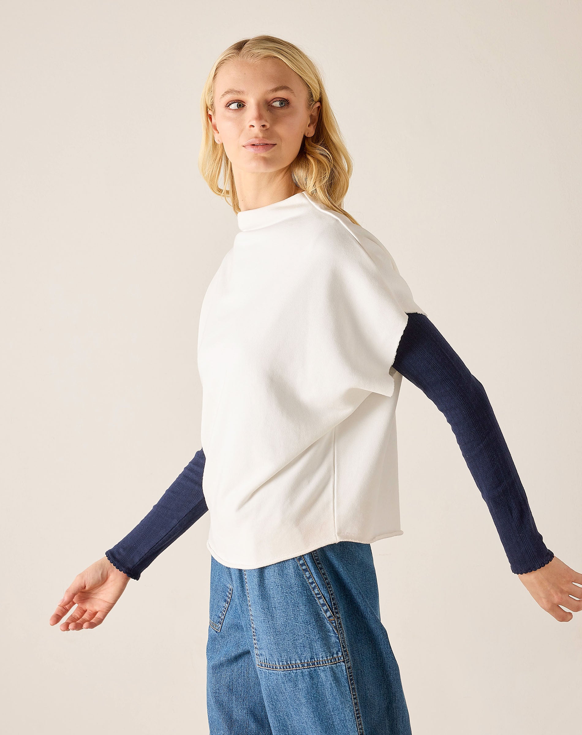 Woman wearing a white top with navy sleeves and blue jeans on a plain background
