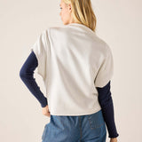 Person wearing a white sweater with navy sleeves and blue jeans on a beige background