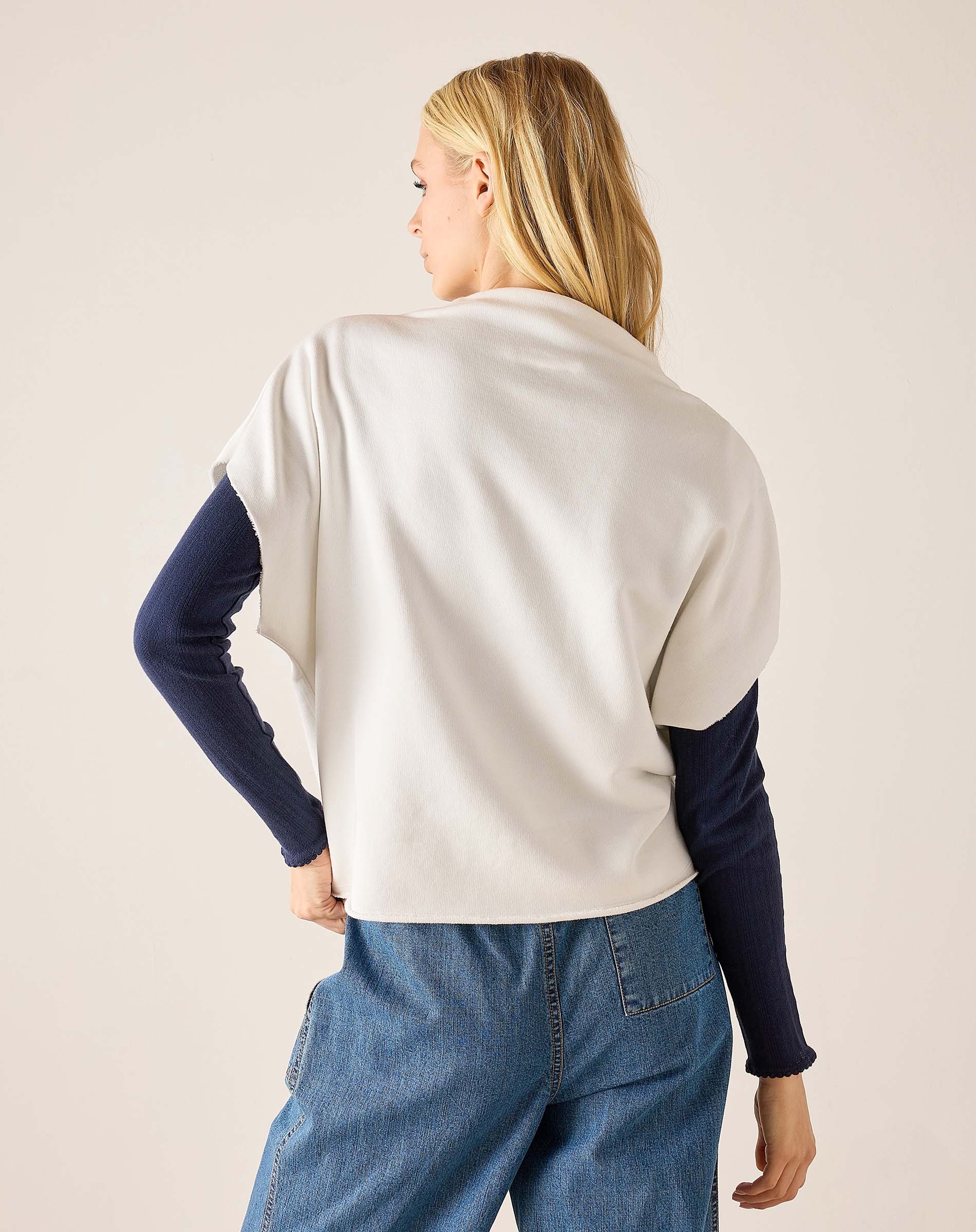 Person wearing a white sweater with navy sleeves and blue jeans on a beige background