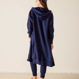 Person wearing a navy blue hooded dress and cap on a beige background