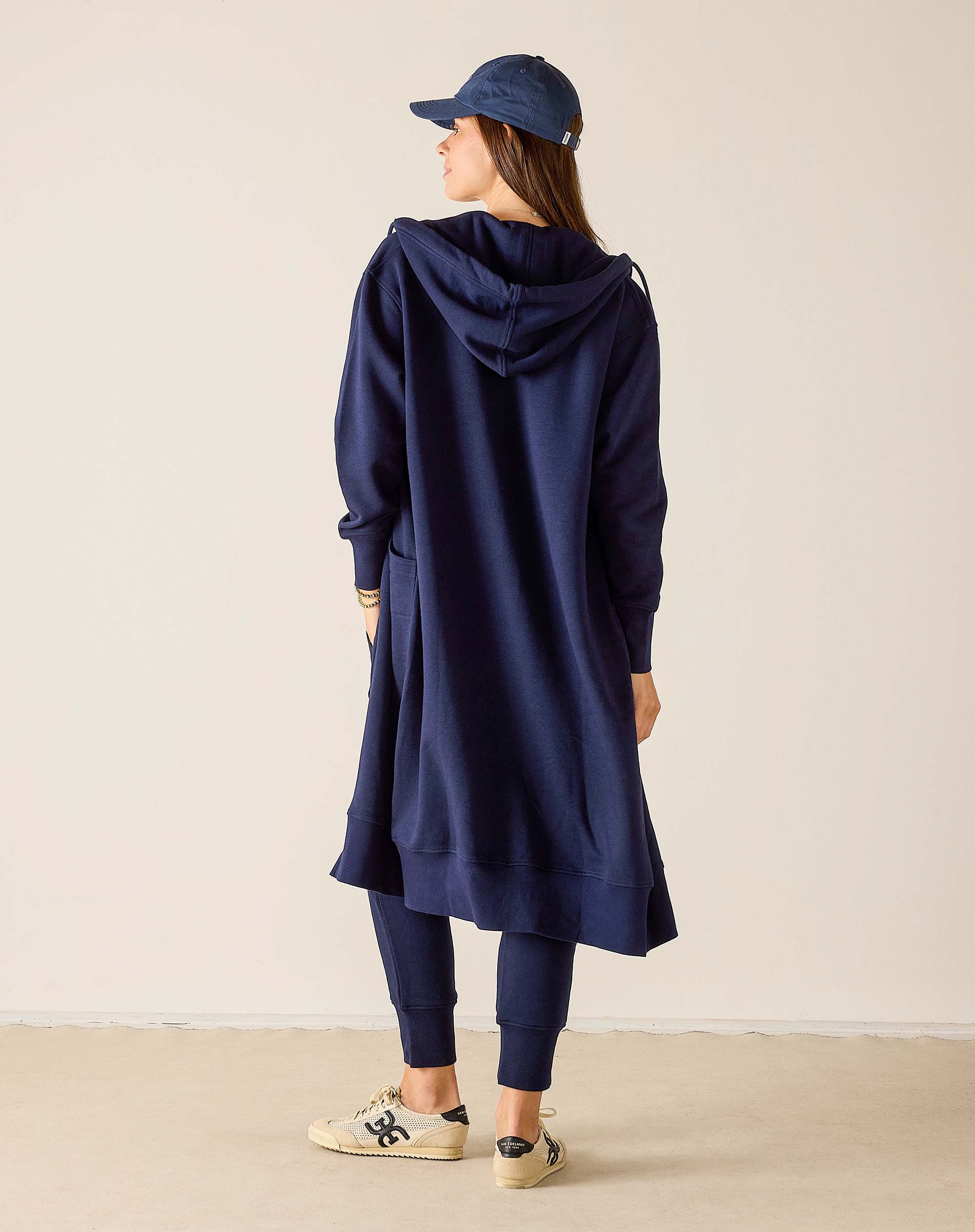 Person wearing a navy blue hooded dress and cap on a beige background