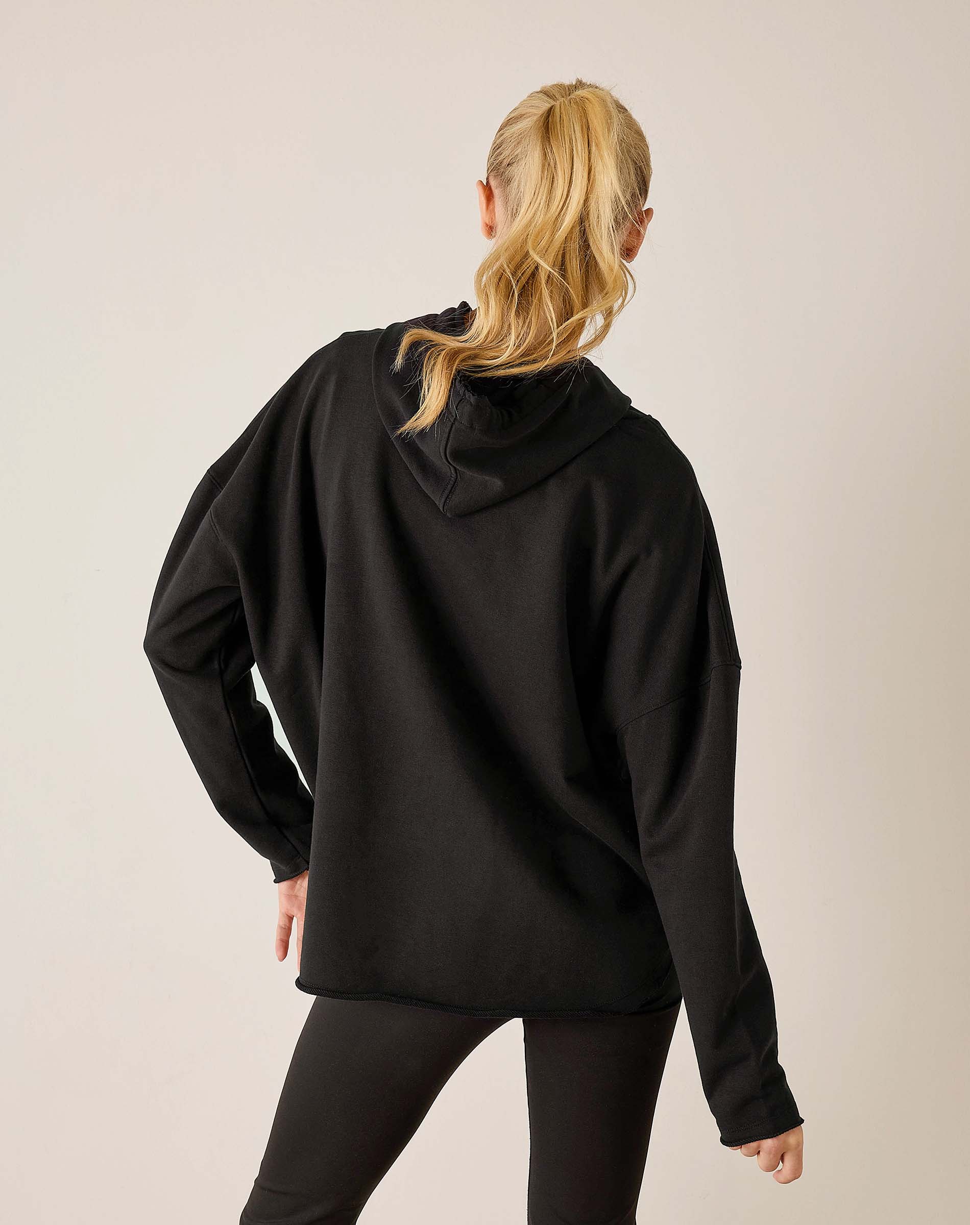 Back view of women's travel-friendly black hoodie with a drawstring hood and dropped shoulders.