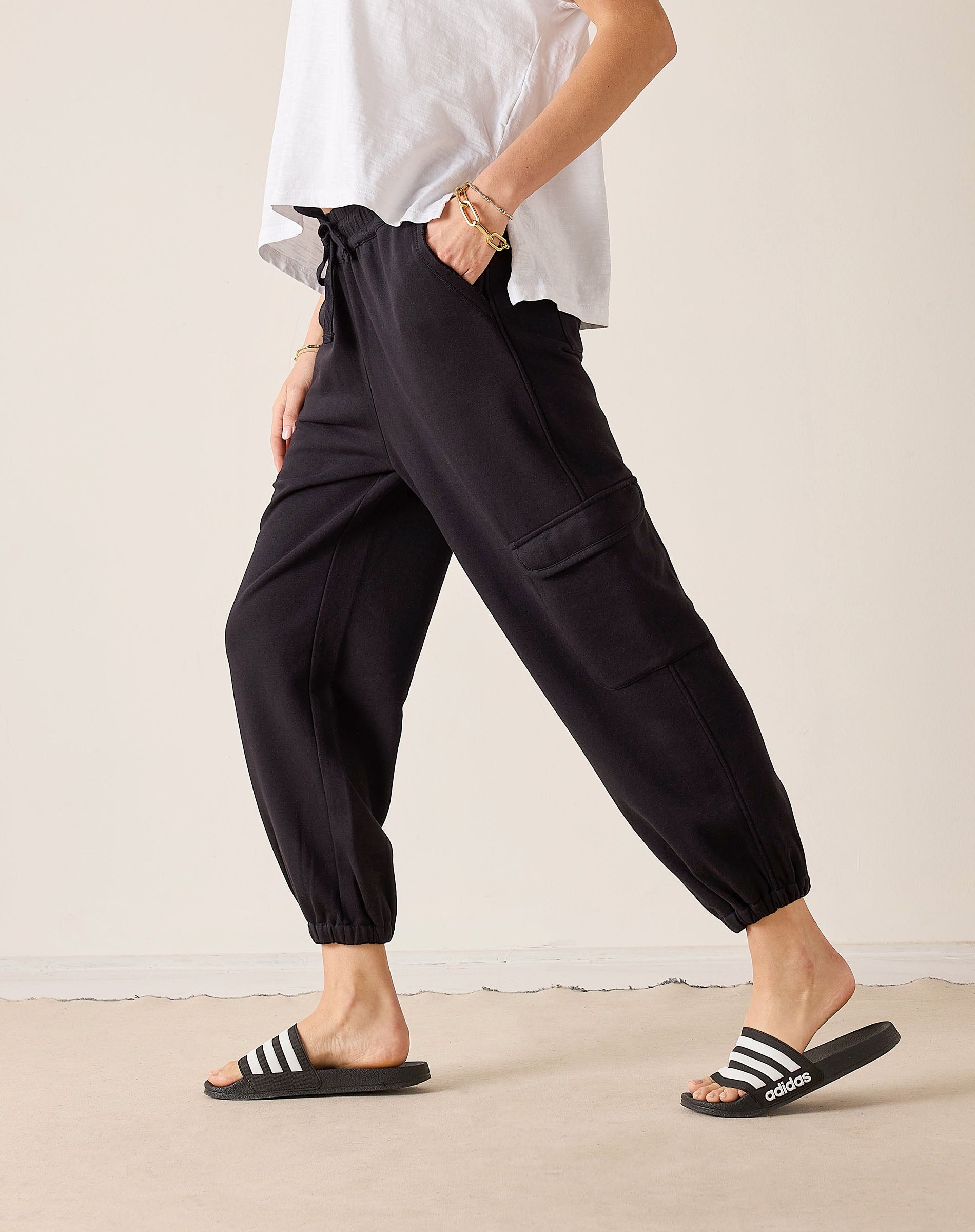 Black jogger-style pants with a cargo pocket and cinched cuffs. Text: adidas