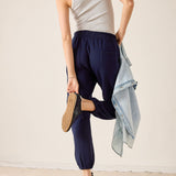 Person wearing navy jogger pants and a striped tank top, holding a denim jacket.