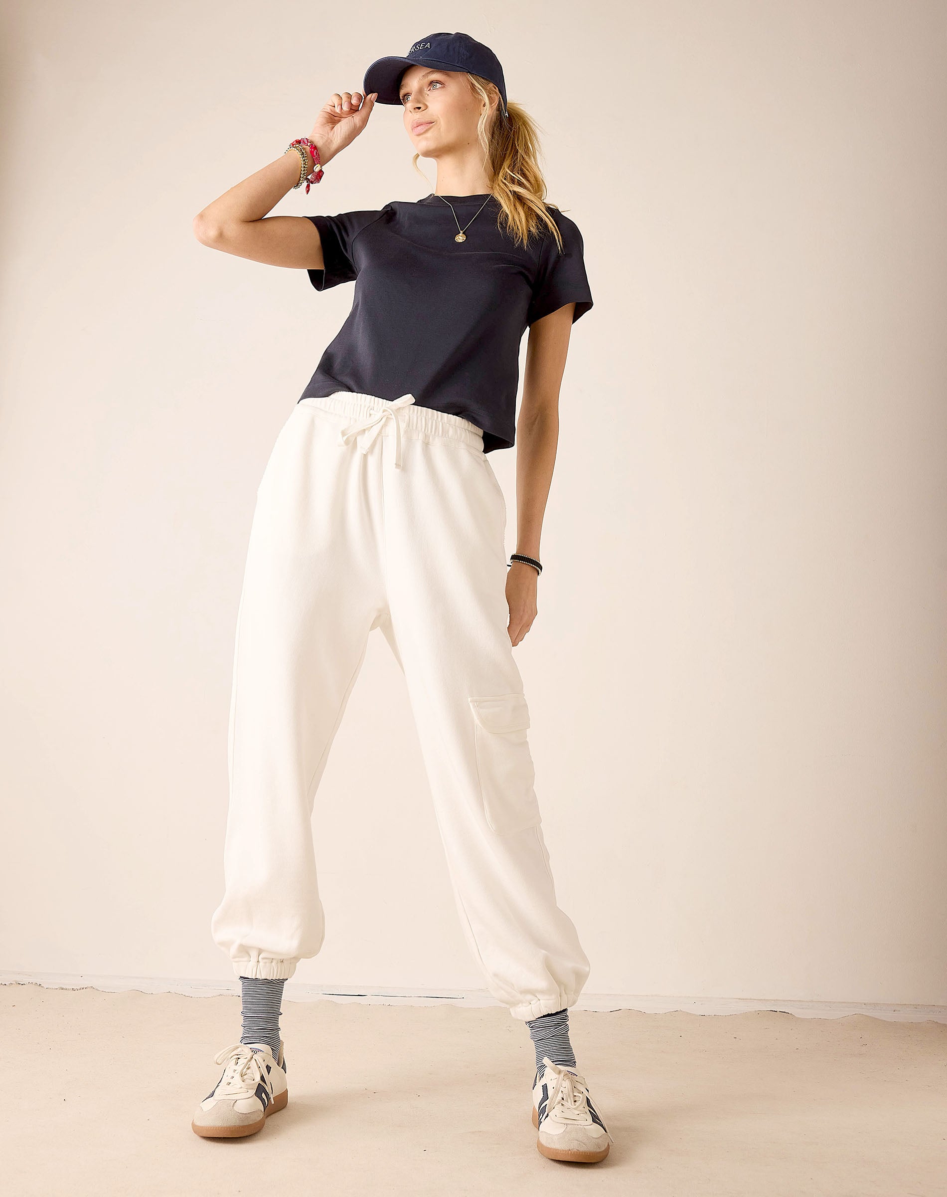 Person wearing a navy t-shirt, white pants, and a cap on a plain background