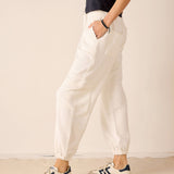 Person wearing white pants and black and white sneakers on a beige background